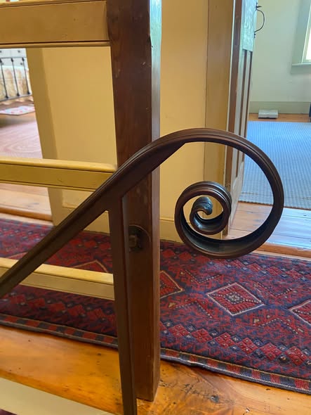 A dark metal railing with a curled end beside a timber post